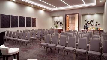 Une salle de conférence avec des rangées de chaises, un comptoir d’accueil et des œuvres d’art décoratives sur les murs.