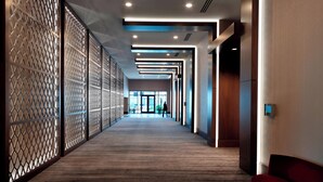 Een moderne hotelgang met een houten vloer, decoratieve lattenpanelen, inbouwverlichting en uitzicht op de lobby.