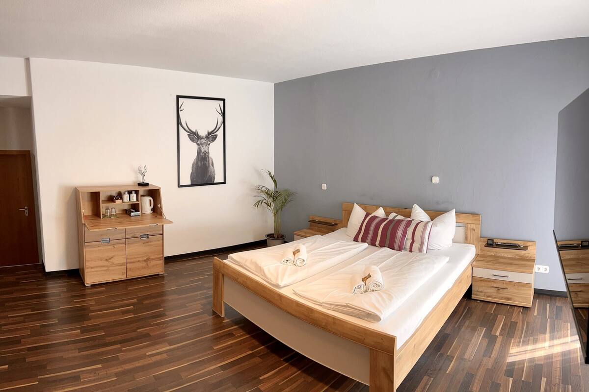 Une chambre moderne avec un lit en bois, une table de chevet, une commode et un tableau représentant une tête de cerf, encadré, accroché au mur.
