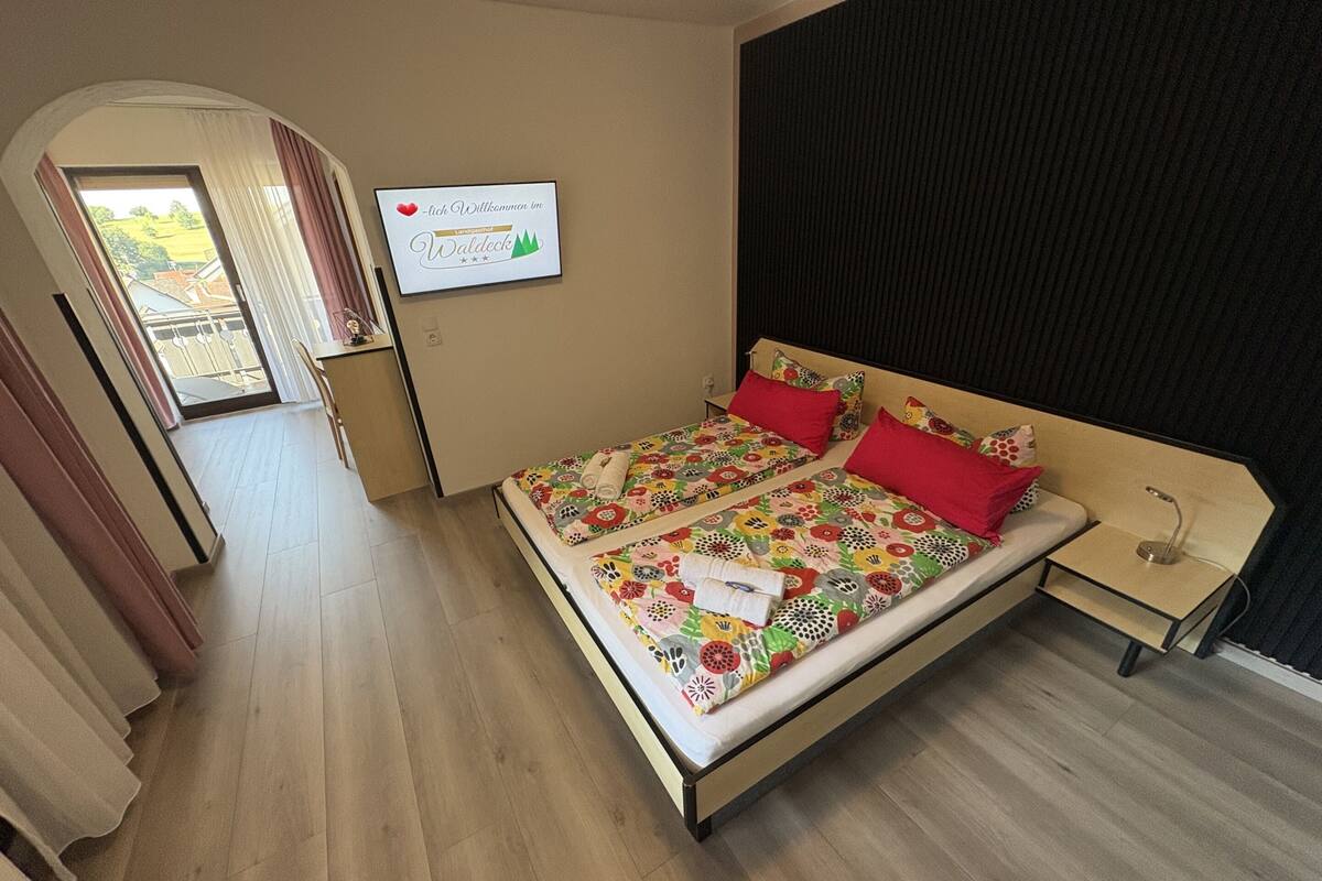 Un lit double avec une literie à motifs floraux, une table de chevet et un panneau accroché au mur.