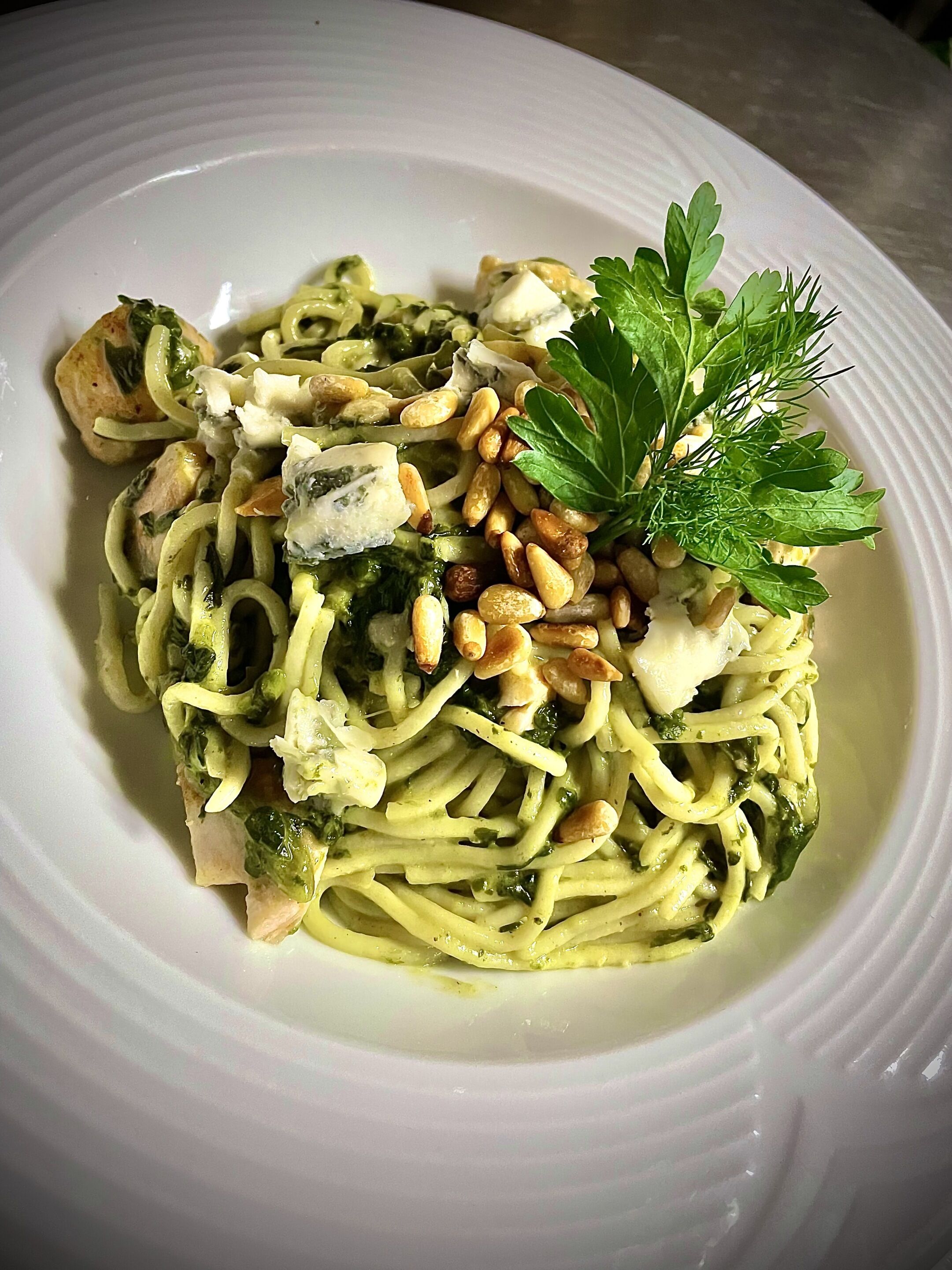 Een bord pasta met pesto, pijnboompitten en een garnering van peterselie.