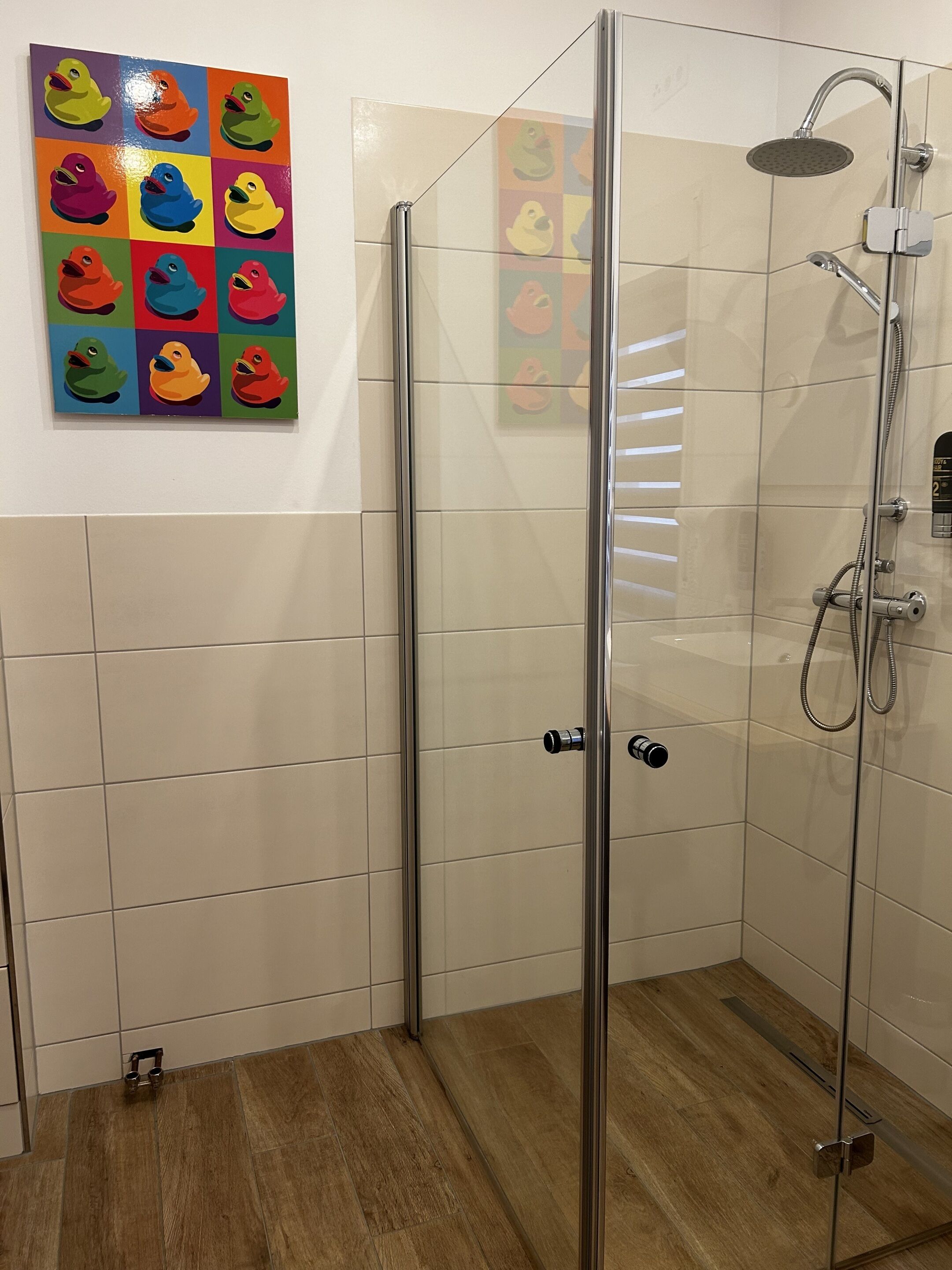 A glass-enclosed shower stall with a handheld showerhead and a wall-mounted control panel.