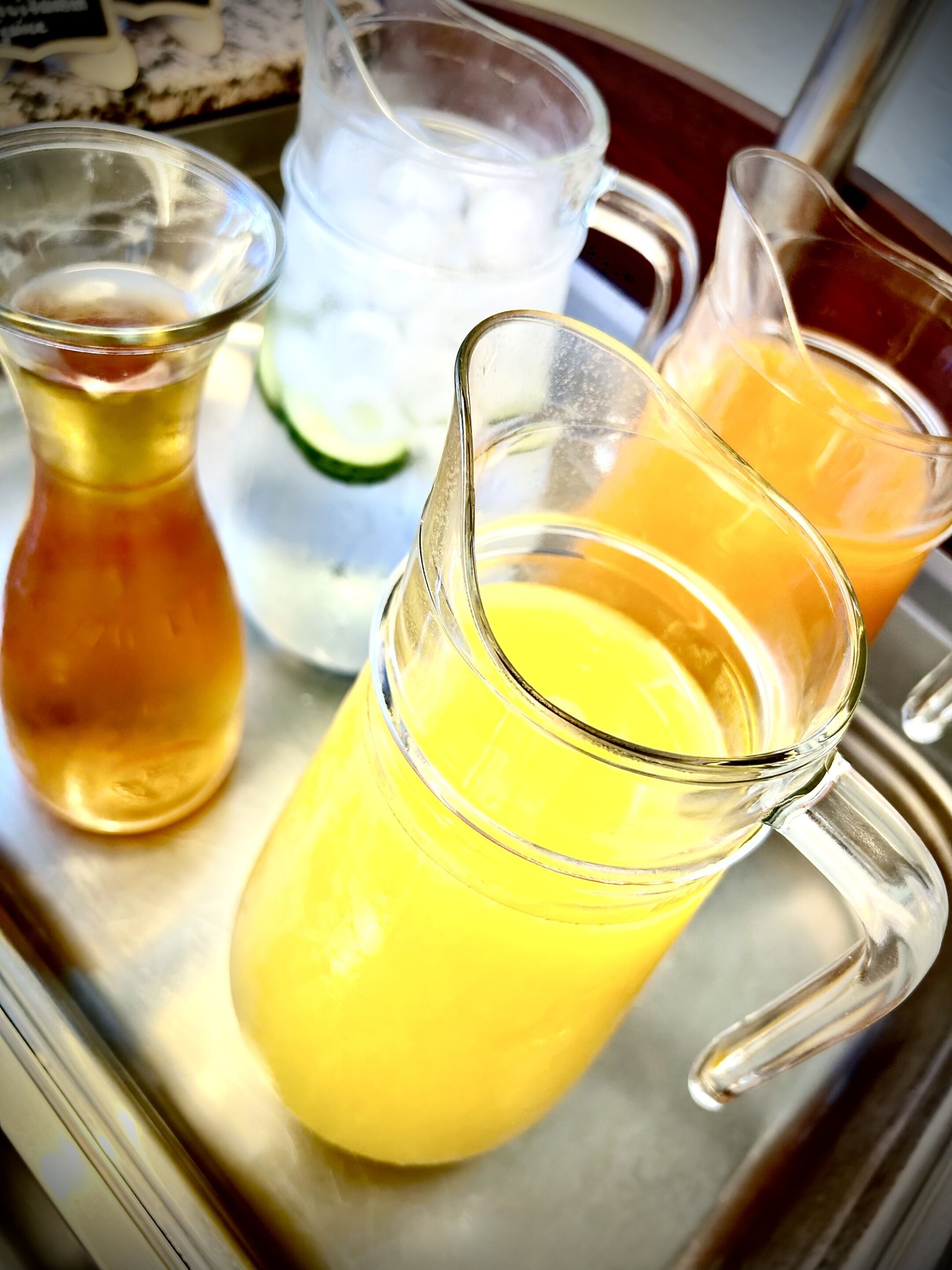 Una bandeja con tres jarras de vidrio llenas de diferentes bebidas.