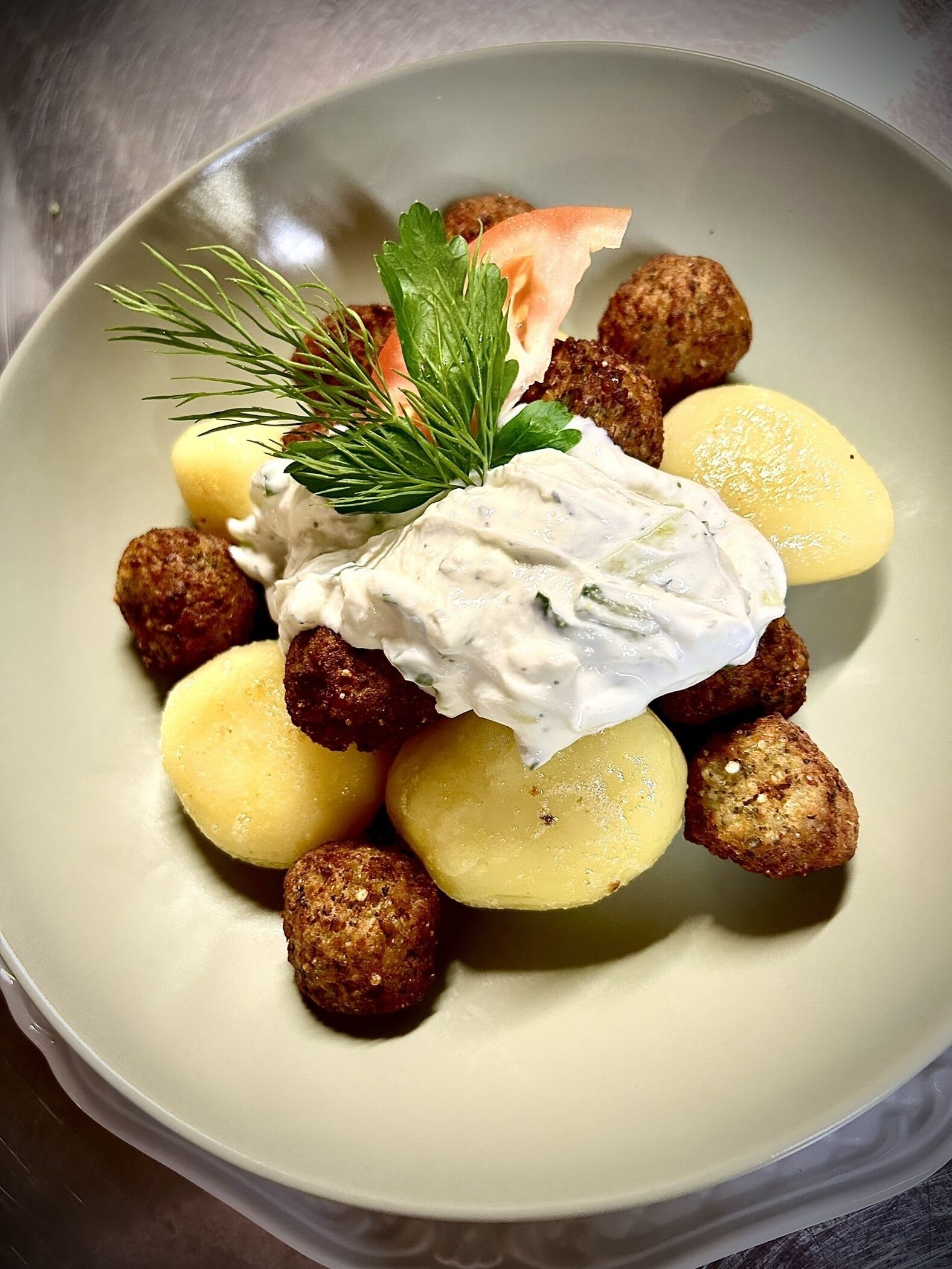 A plate with fried balls, boiled potatoes, and a dollop of white sauce, garnished with a sprig of dill.