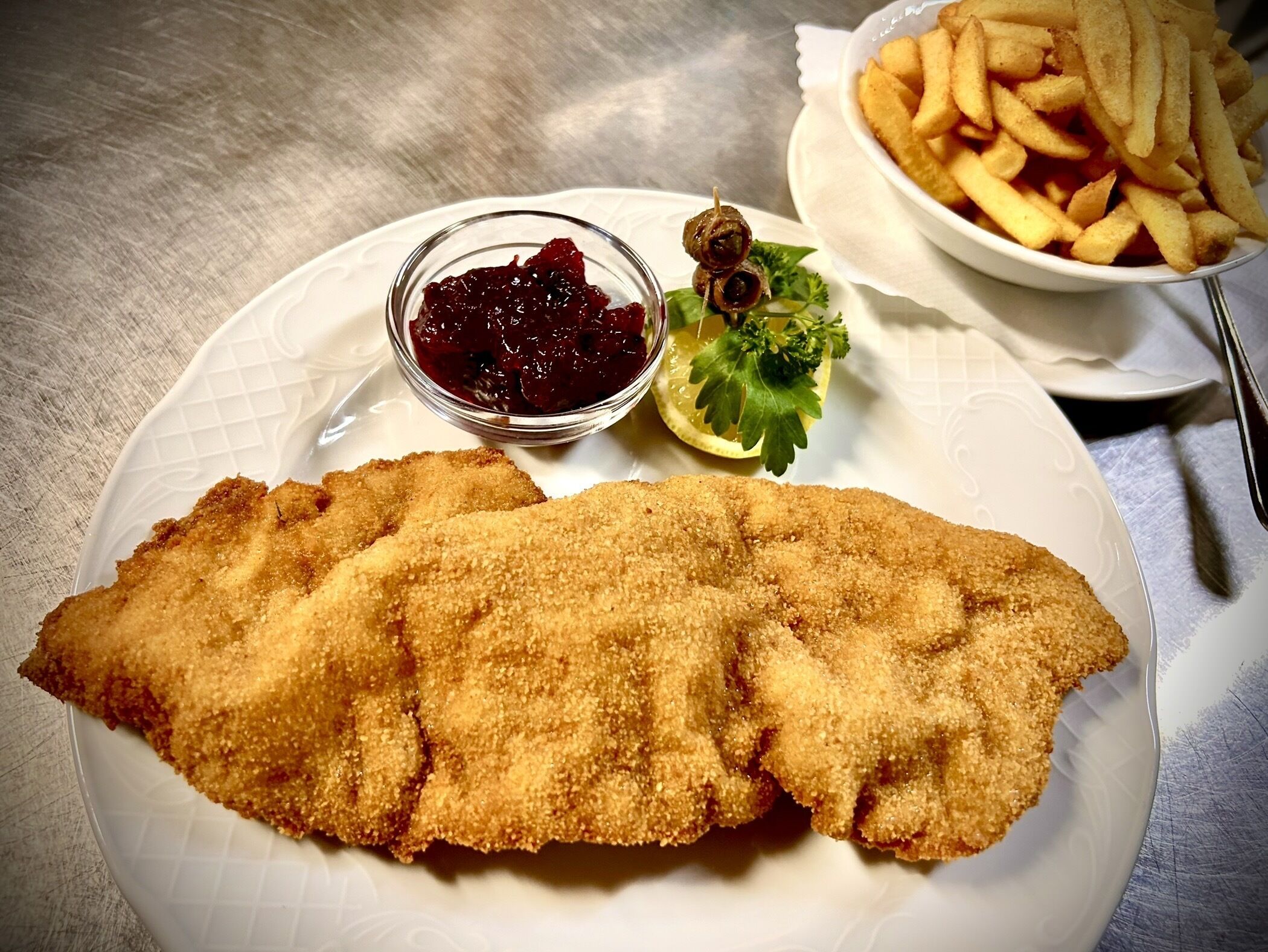 A plate with a breaded fish fillet, a bowl of red sauce, and a side of French fries.