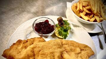 A plate with a breaded fish fillet, a bowl of red sauce, and a side of French fries.