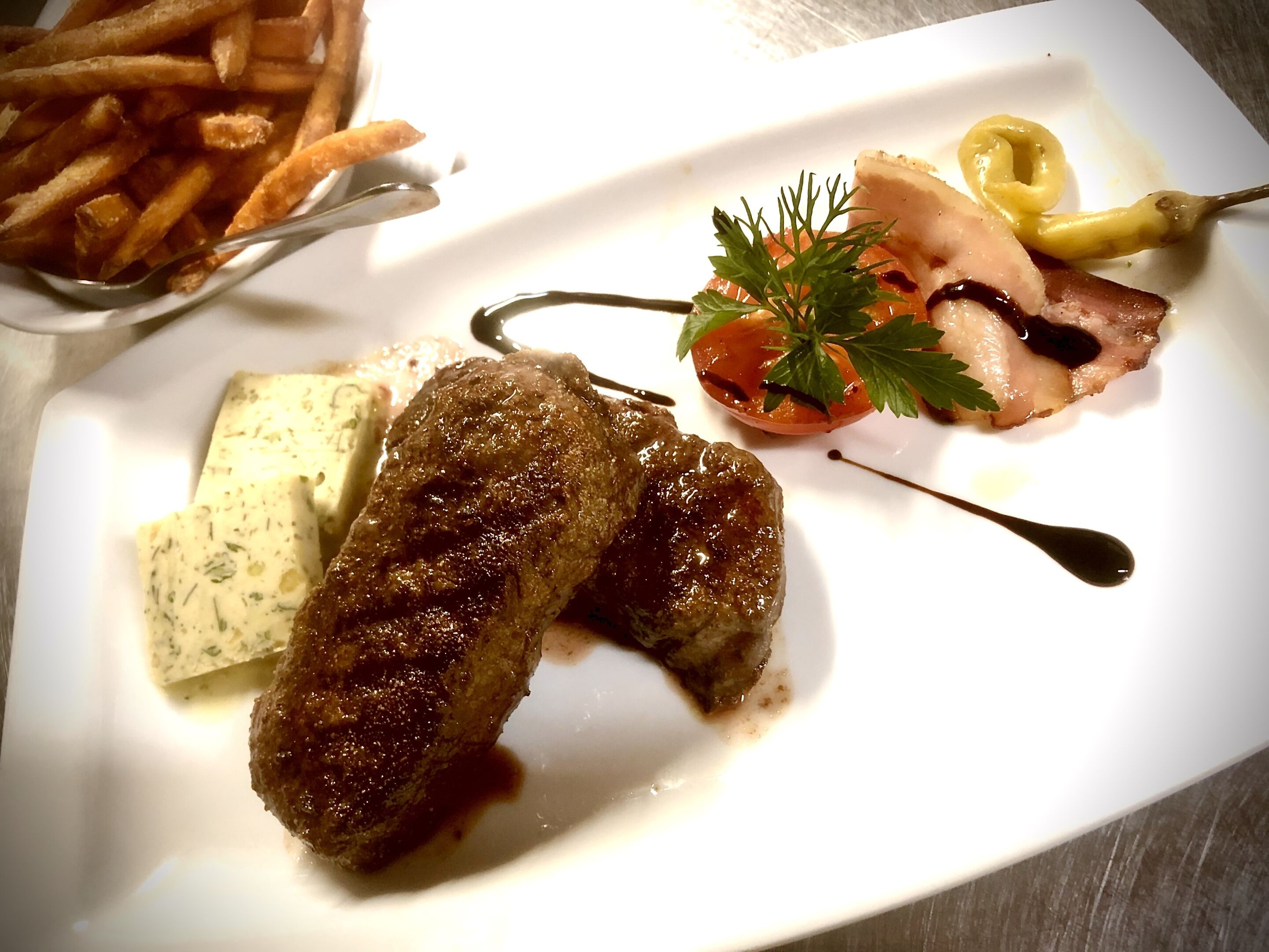 Un plato con carne a la parrilla, una rebanada de queso, un tomate pequeño y papas fritas.