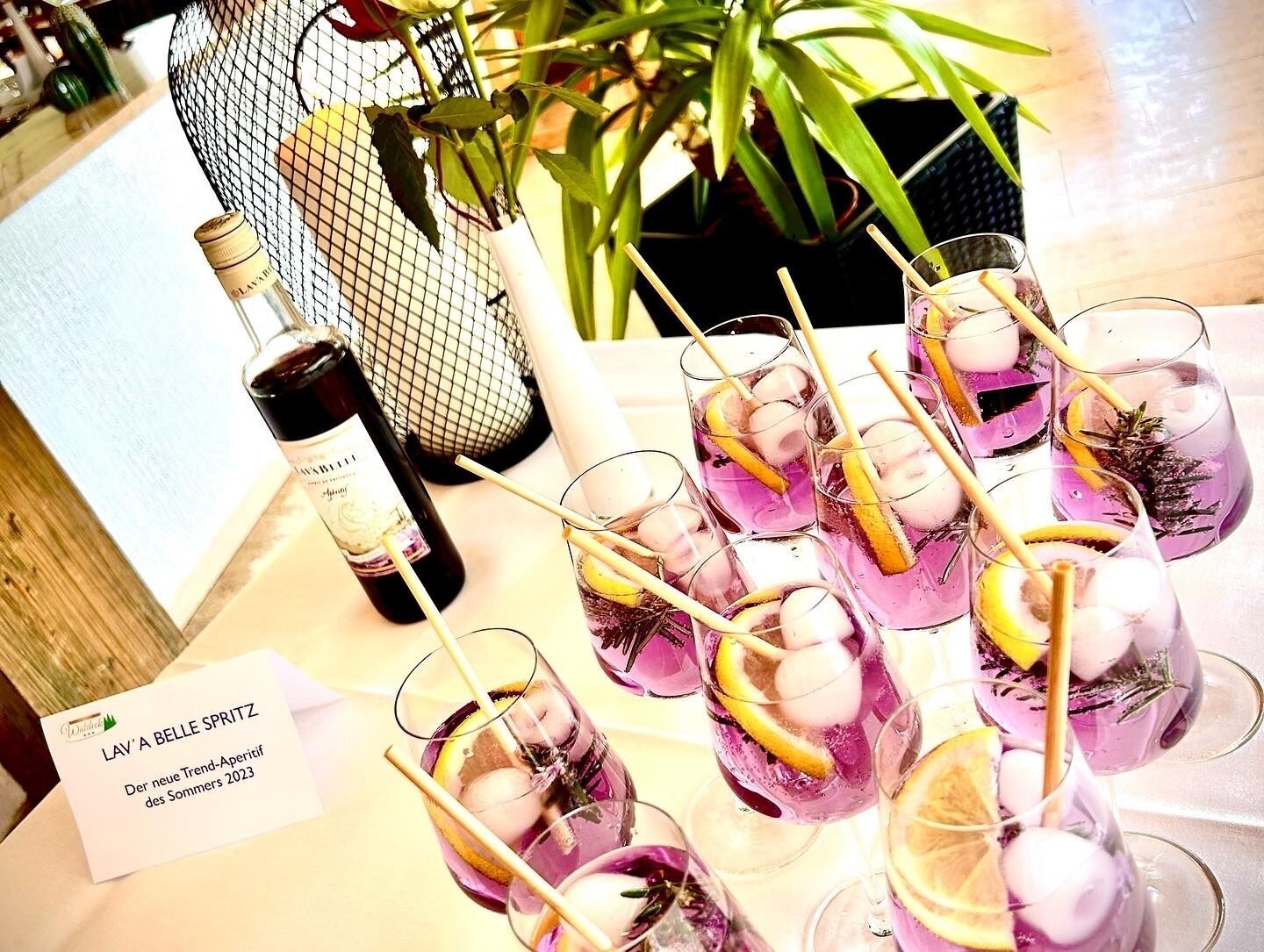 A table with several glasses of a purple beverage, a bottle of wine, and a sign reading "LAV' A BELLE SPRITZ".