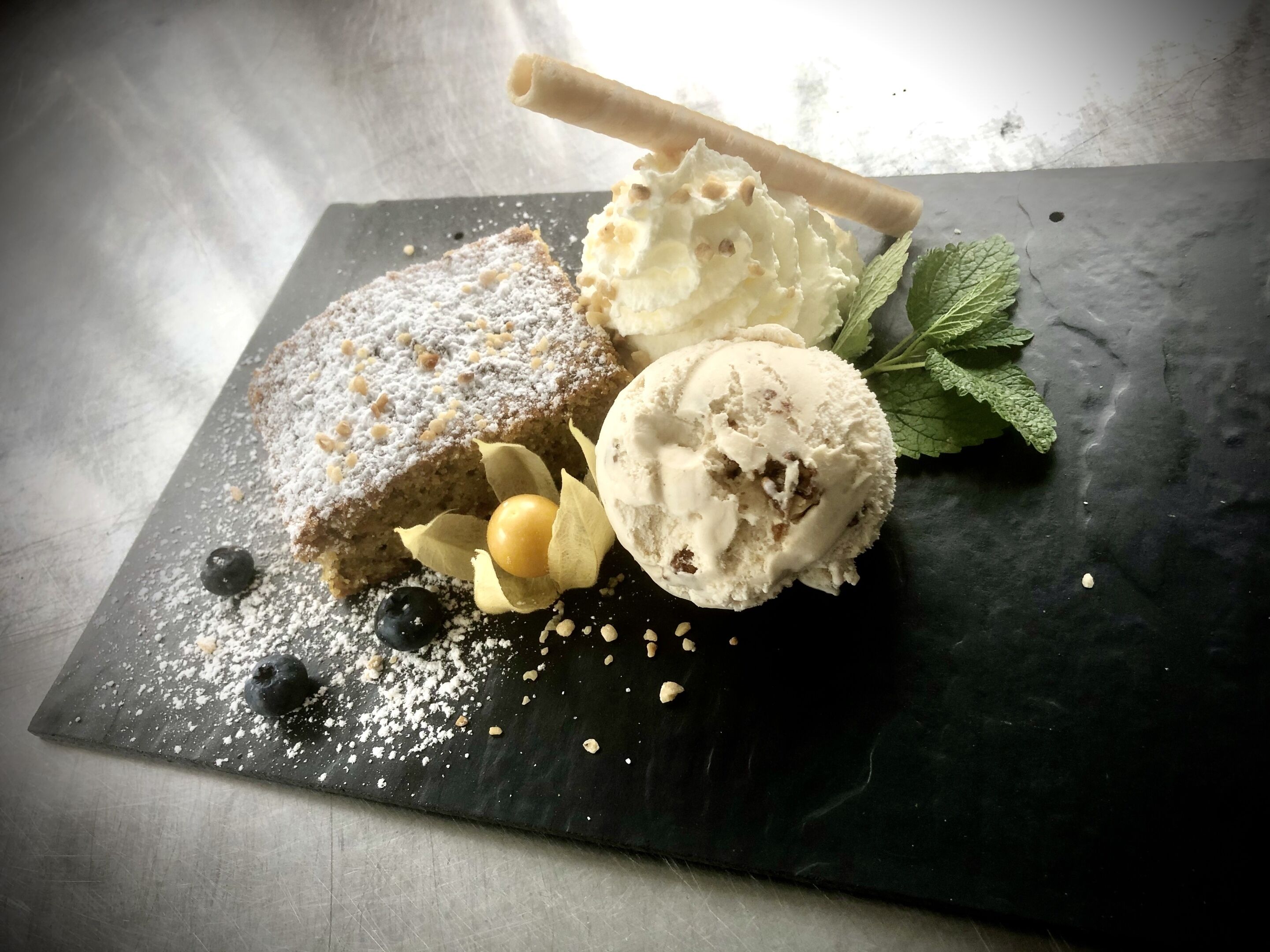 Un plato de postre con pastel, helado y bayas sobre una tabla de pizarra.