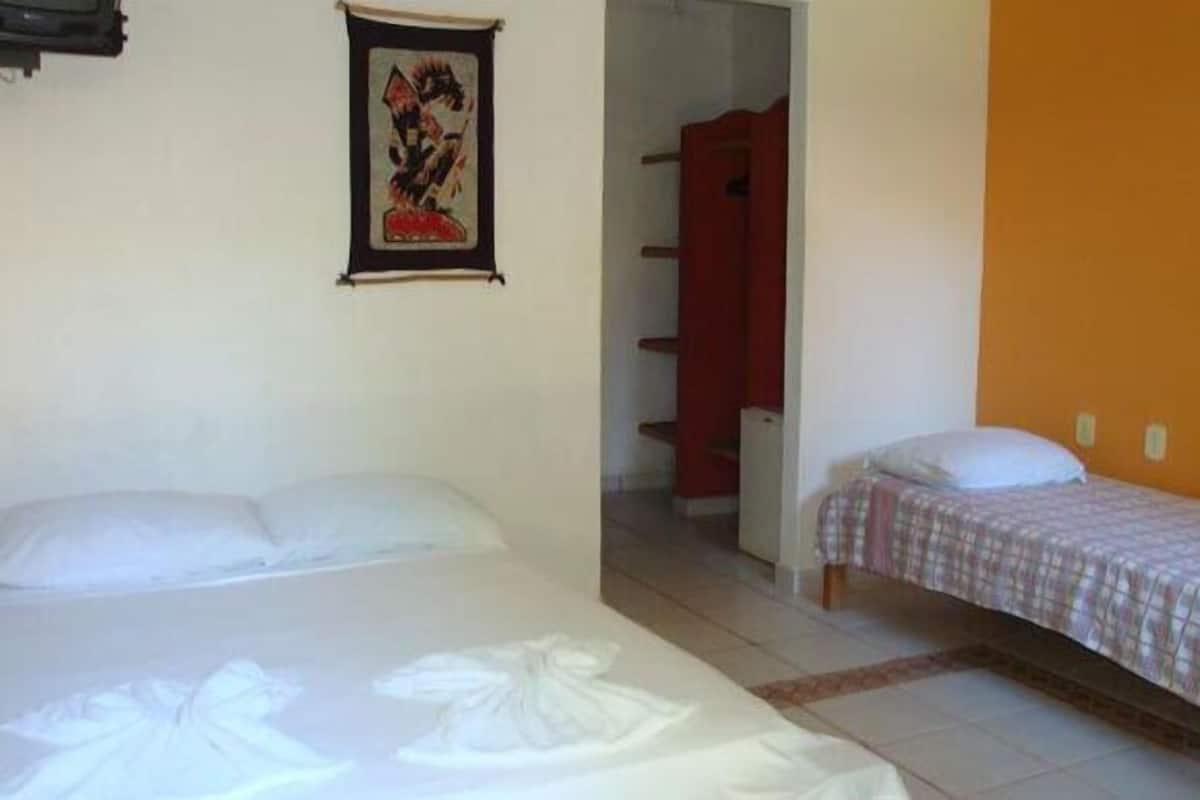 A room with two beds, one larger and one smaller, a red wardrobe, and a framed picture on the wall.