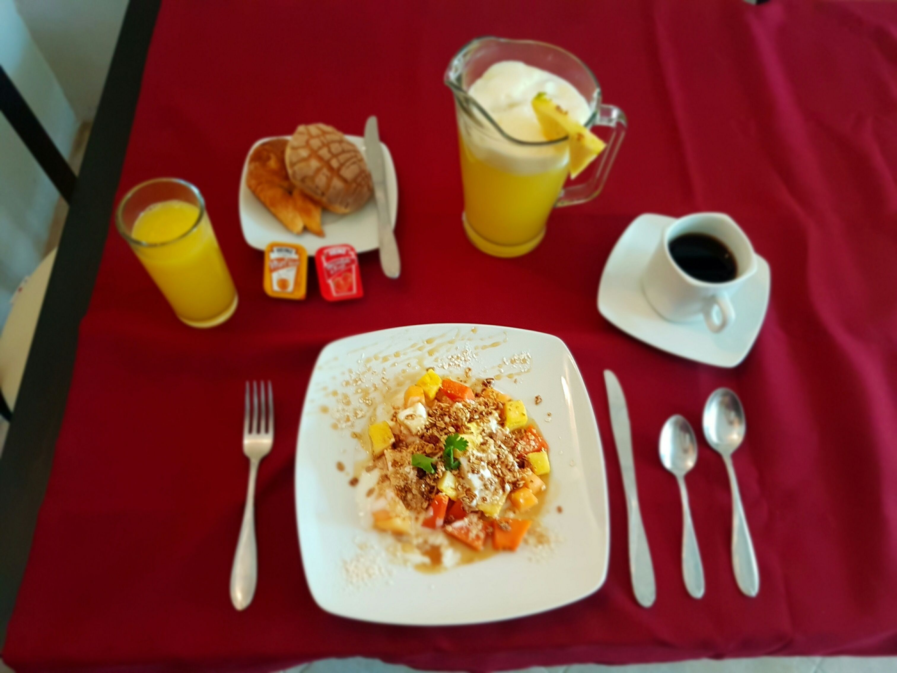 A breakfast table with a plate of food, a glass of orange juice, a pitcher of orange juice, a cup of coffee, and condiments.