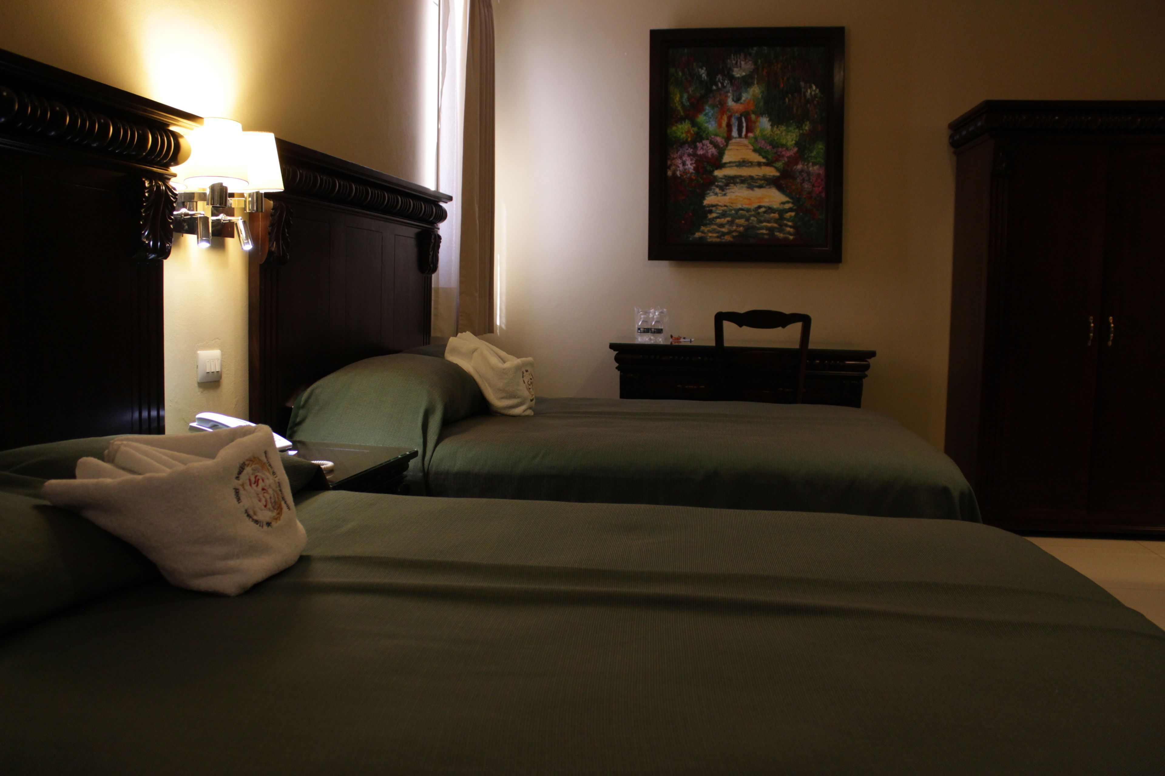 Habitación de hotel con dos camas, un cuadro en la pared y una mesita de noche con una lámpara.