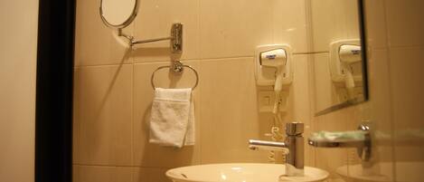 Un baño con un lavabo, una toalla colgada en un perchero, un espejo y un secador de pelo en la pared.