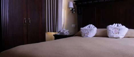 A hotel room with a large bed, a nightstand with a lamp, and two towels on the bed.