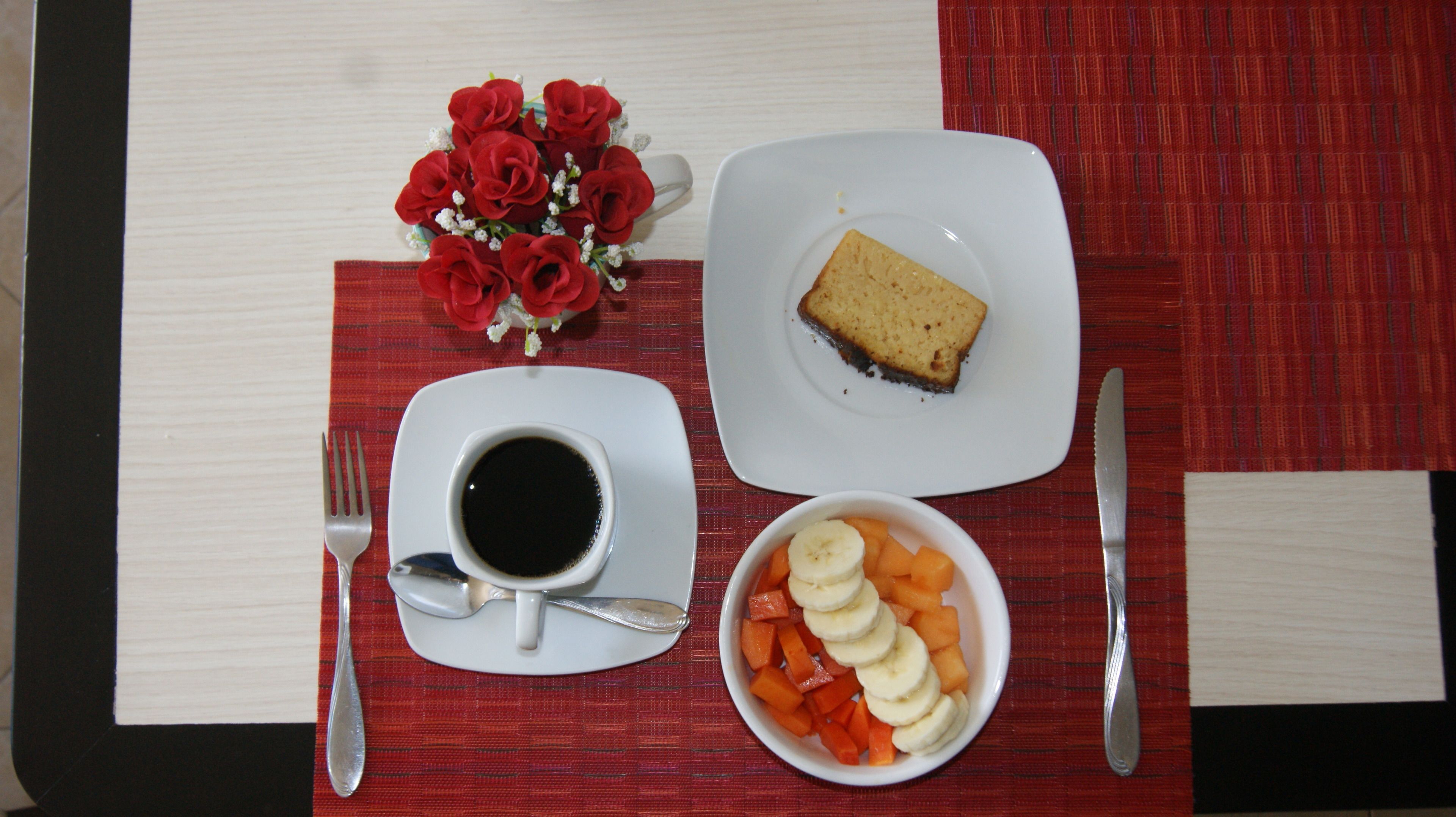 A table setting with a plate of cheesecake, a bowl of fruit, and a cup of coffee.