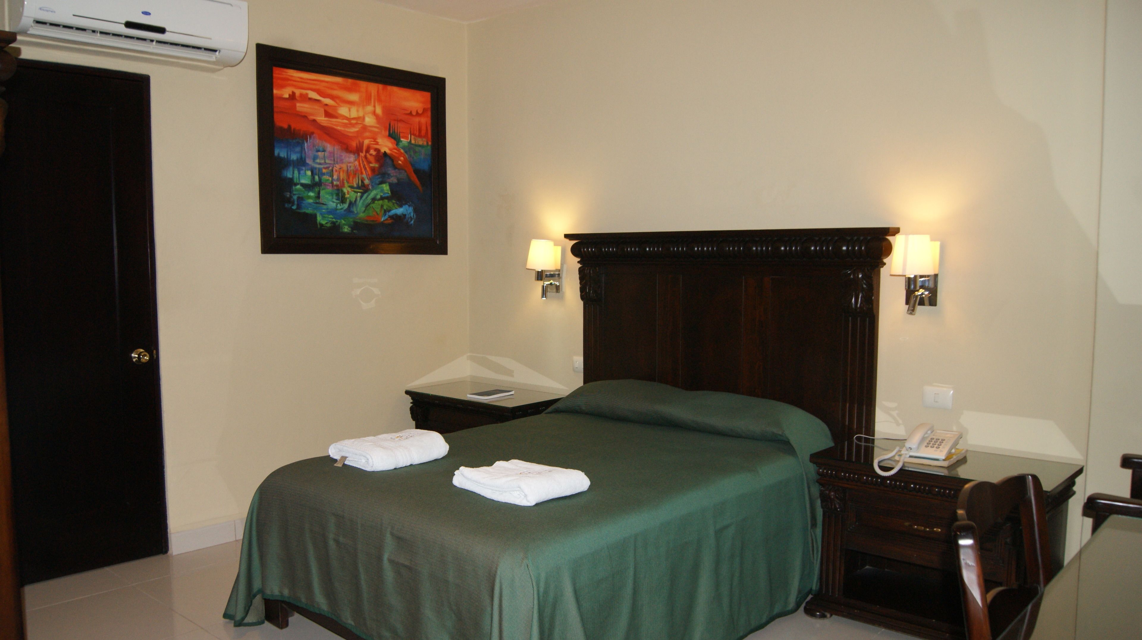 A hotel room with a bed, a nightstand, a telephone, and a painting on the wall.