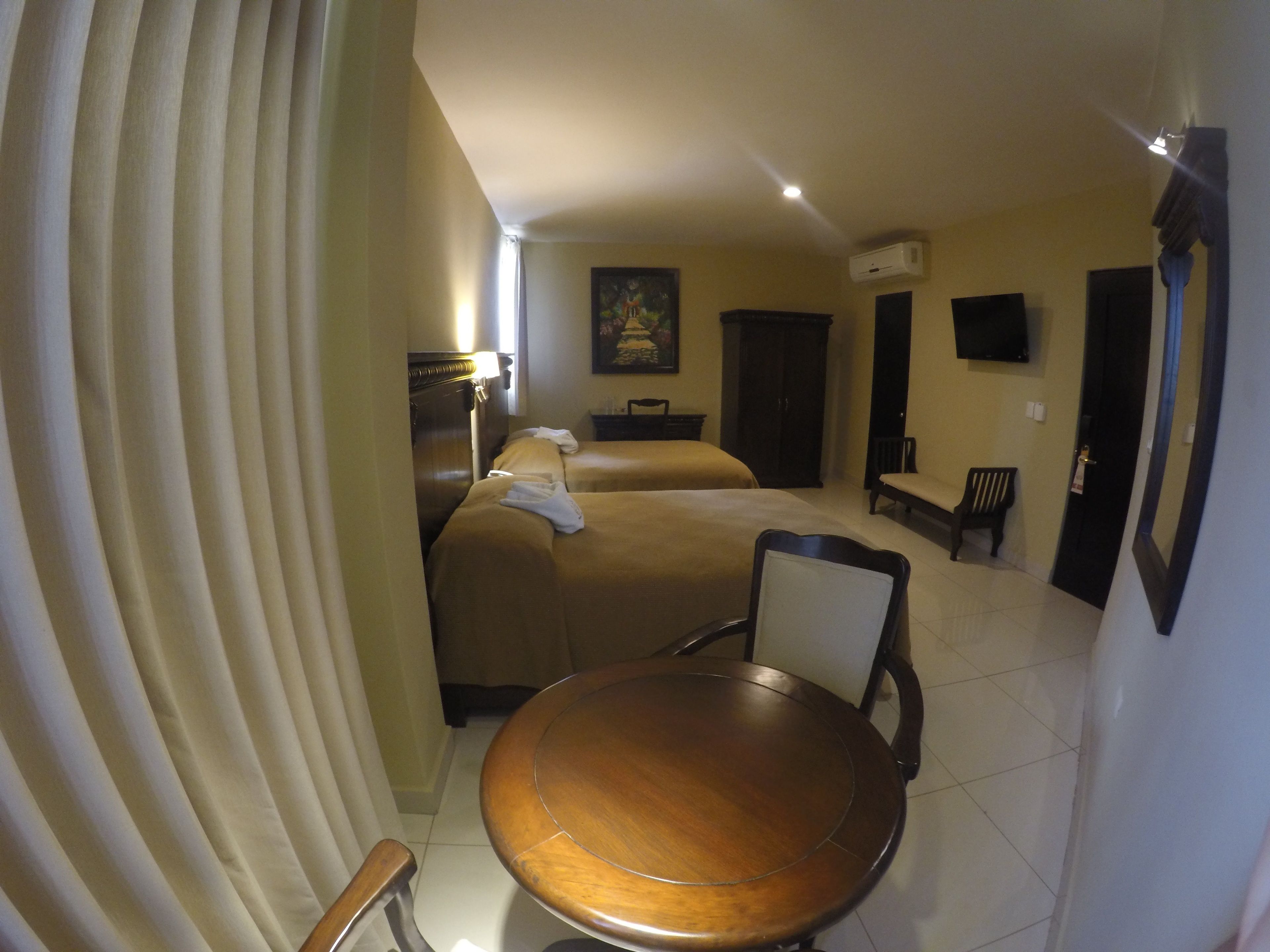 Habitación de hotel con dos camas, una mesa de comedor de madera, una silla, un televisor y un equipo de aire acondicionado.
