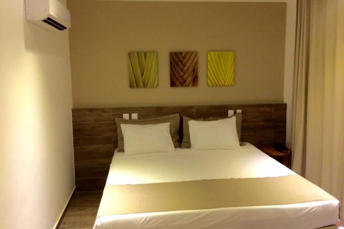 A hotel room with a large bed, a wooden headboard, and three wall-mounted decorative panels.