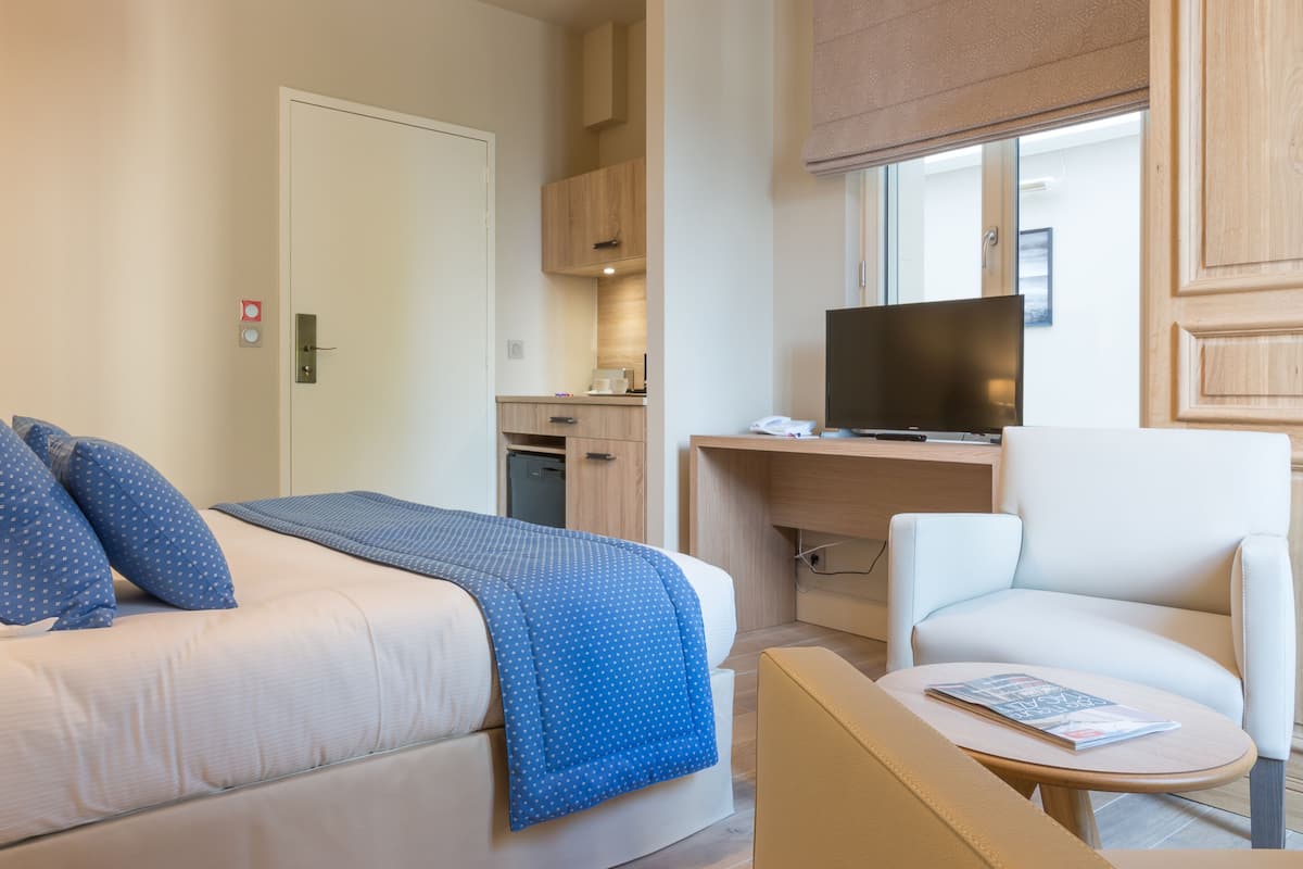 A hotel room with a bed, a desk with a computer, a chair, and a small table with a magazine.