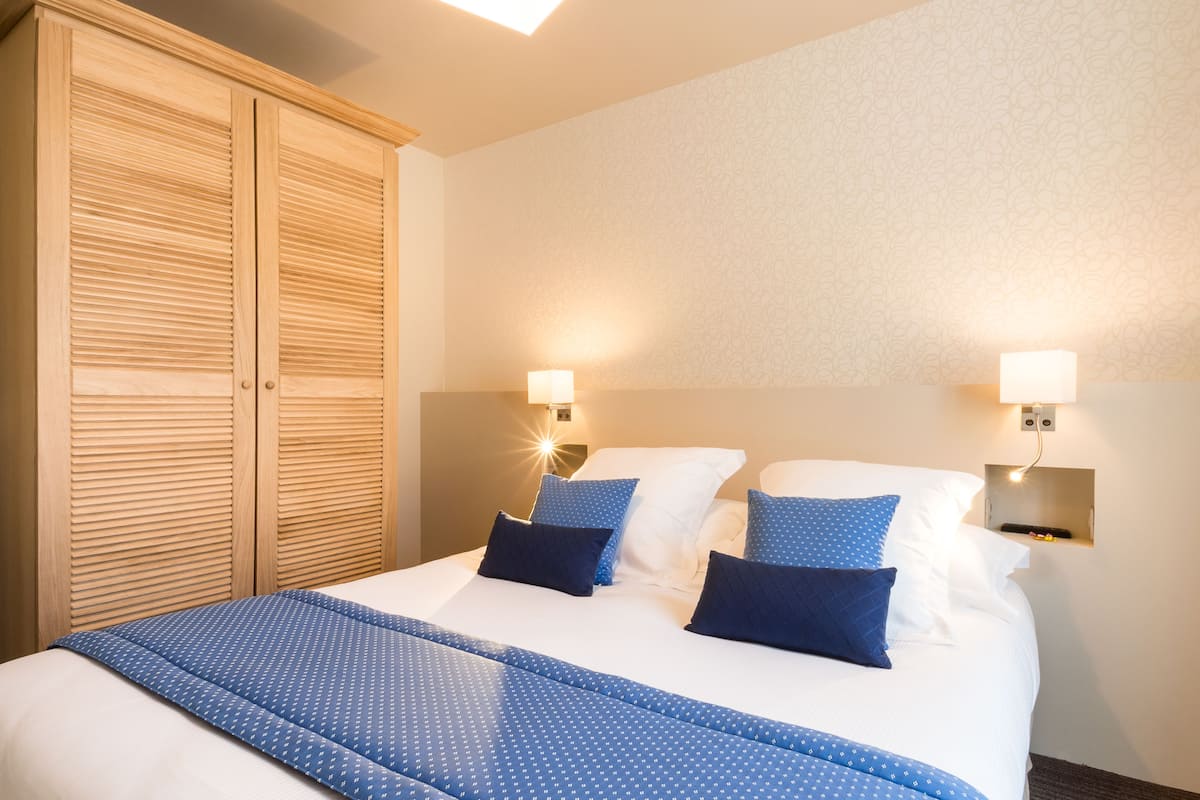 A hotel room with a large bed, two wall-mounted lamps, and a wooden wardrobe.