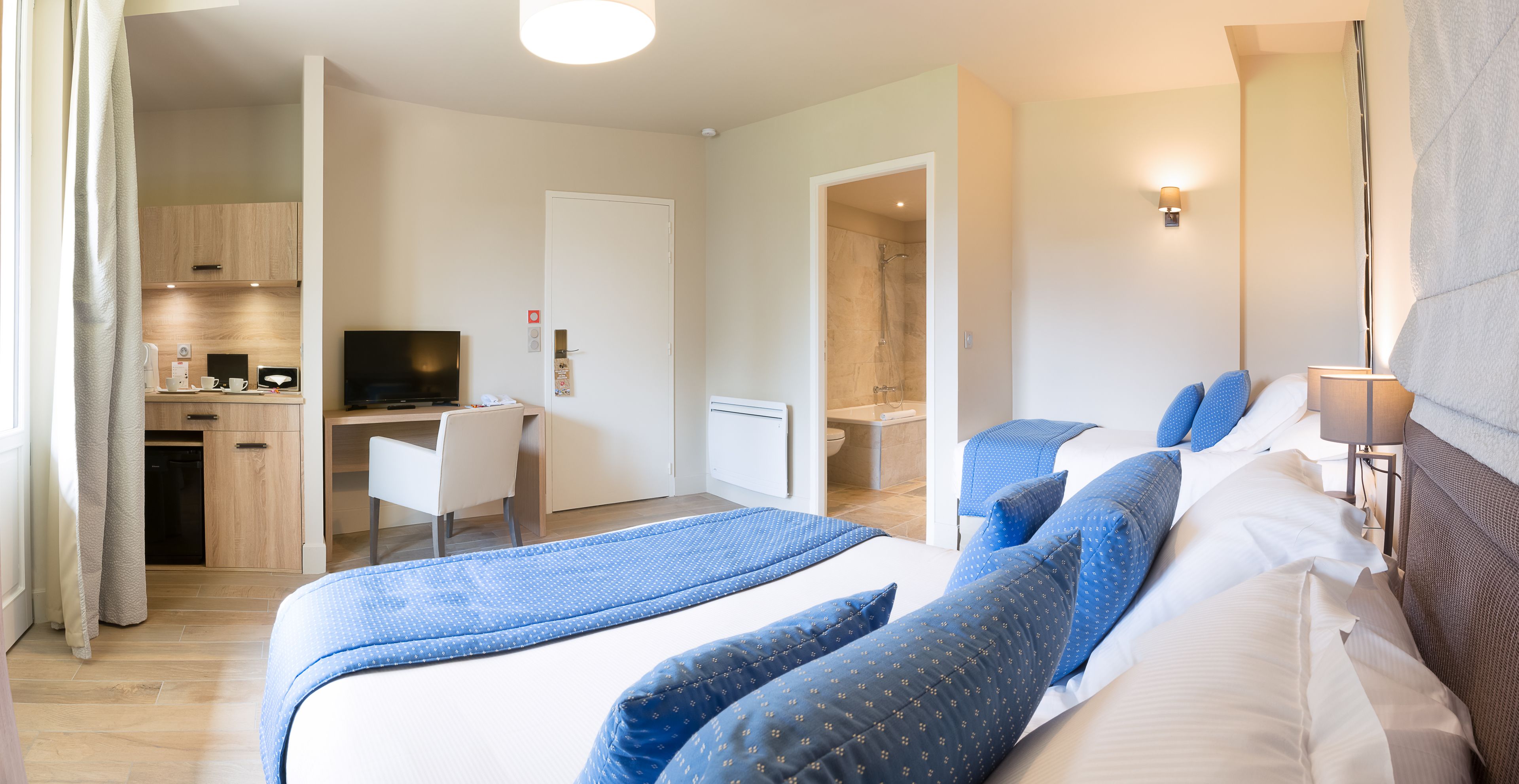 A hotel room with a bed, a desk, a TV, and a bathroom.