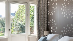 Un dormitorio con cama, cortinas, ventana y pared con estampado de lunares.