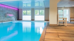 Una piscina interior con paredes de vidrio transparente, piso de madera y una cascada.
