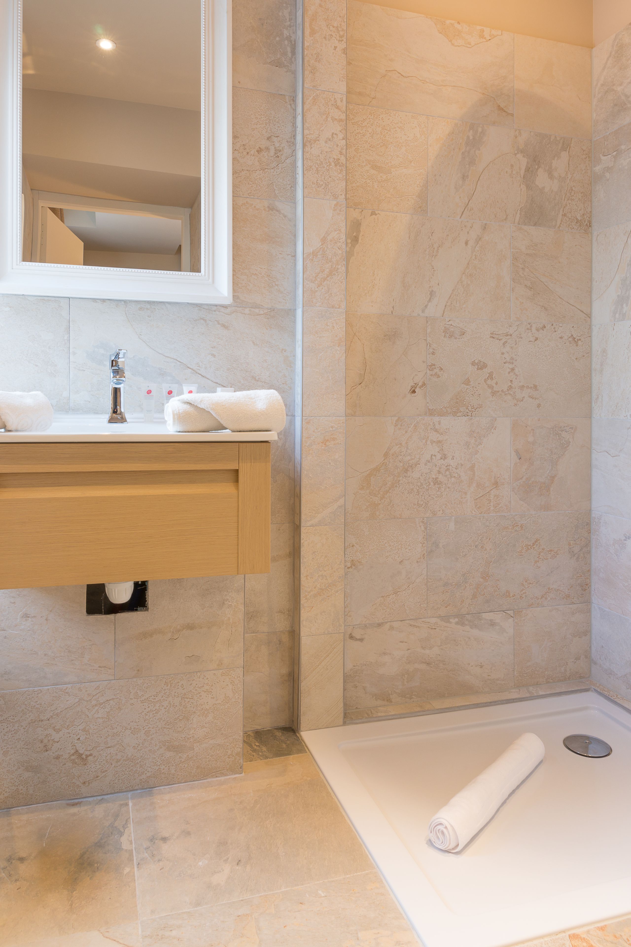 A bathroom with a marble wall, a wooden vanity, and a shower area.