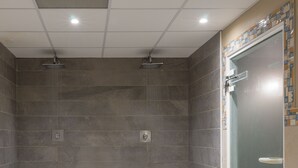 Un área de ducha con paredes y suelo de baldosas, una puerta de cristal e iluminación empotrada en el techo.