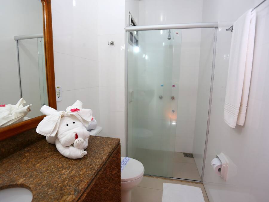 Un baño con ducha de vidrio, encimera de mármol, inodoro blanco y un peluche en la encimera.