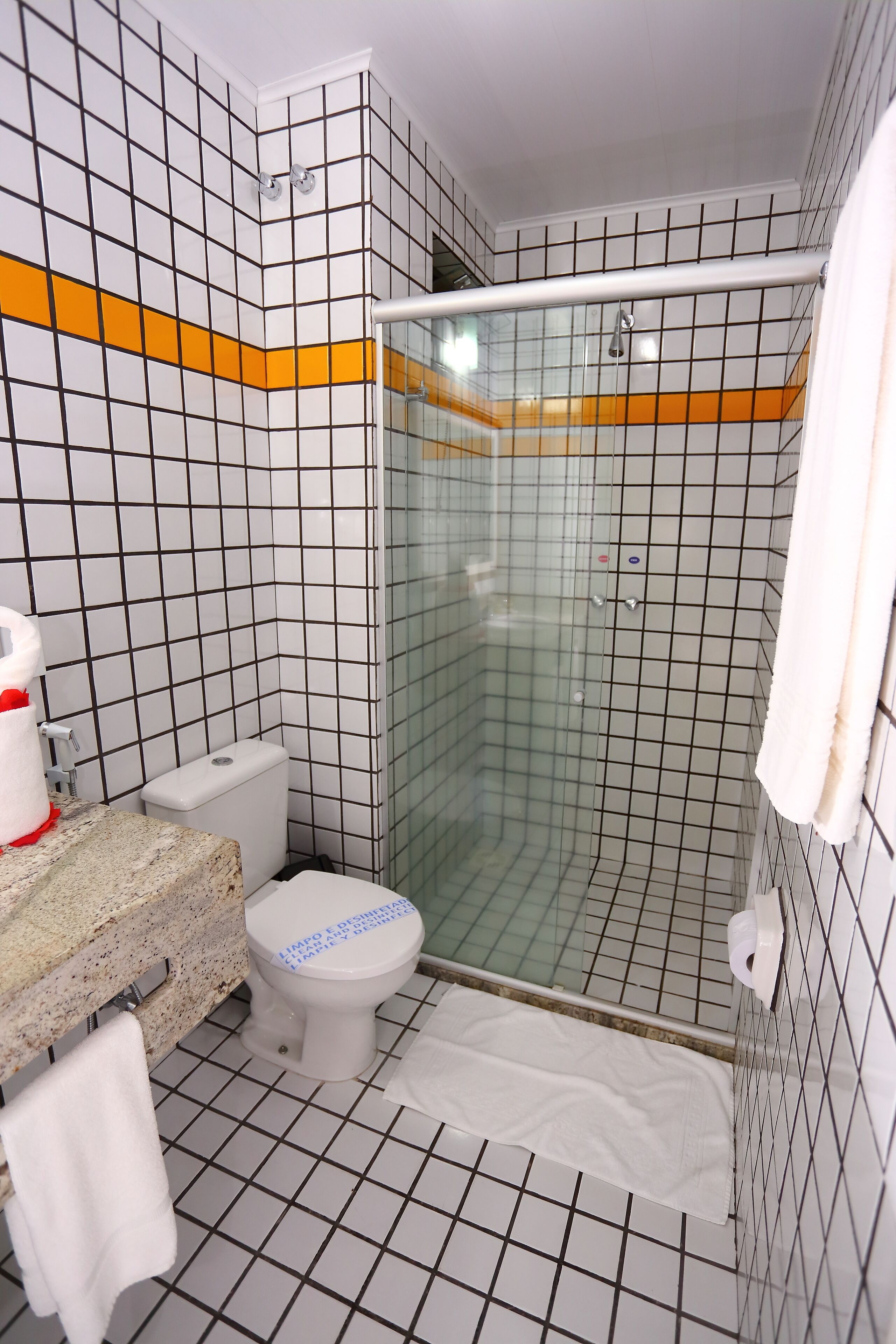 A bathroom with a tiled floor, a toilet, a shower with a glass door, and a sink with a towel hanging on the wall.
