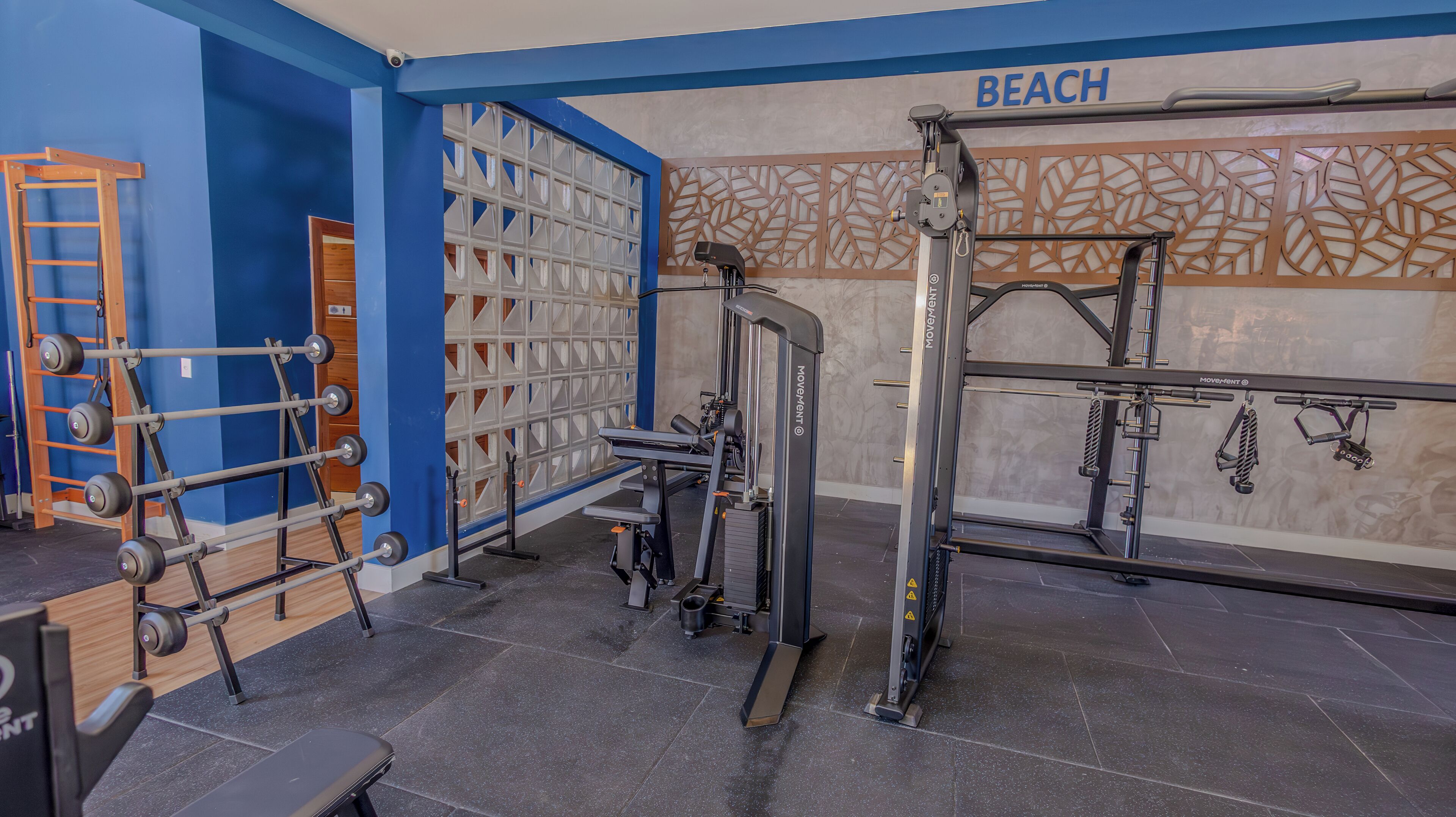 A gym with various exercise equipment, a wooden ladder, and a wall with a 'BEACH' sign.