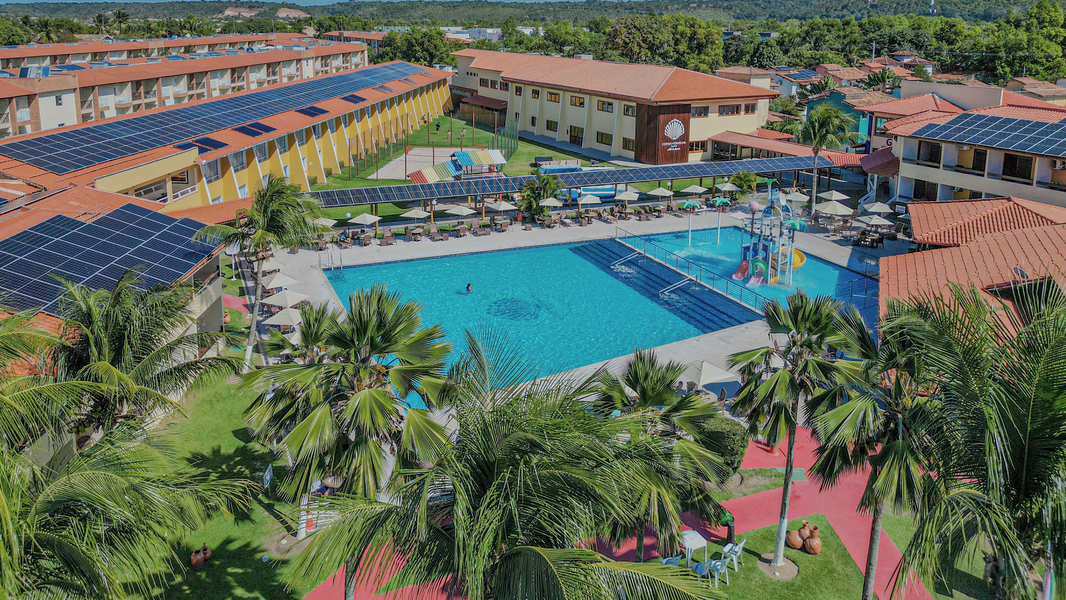 A resort with a central swimming pool, multiple buildings with solar panels, and palm trees.