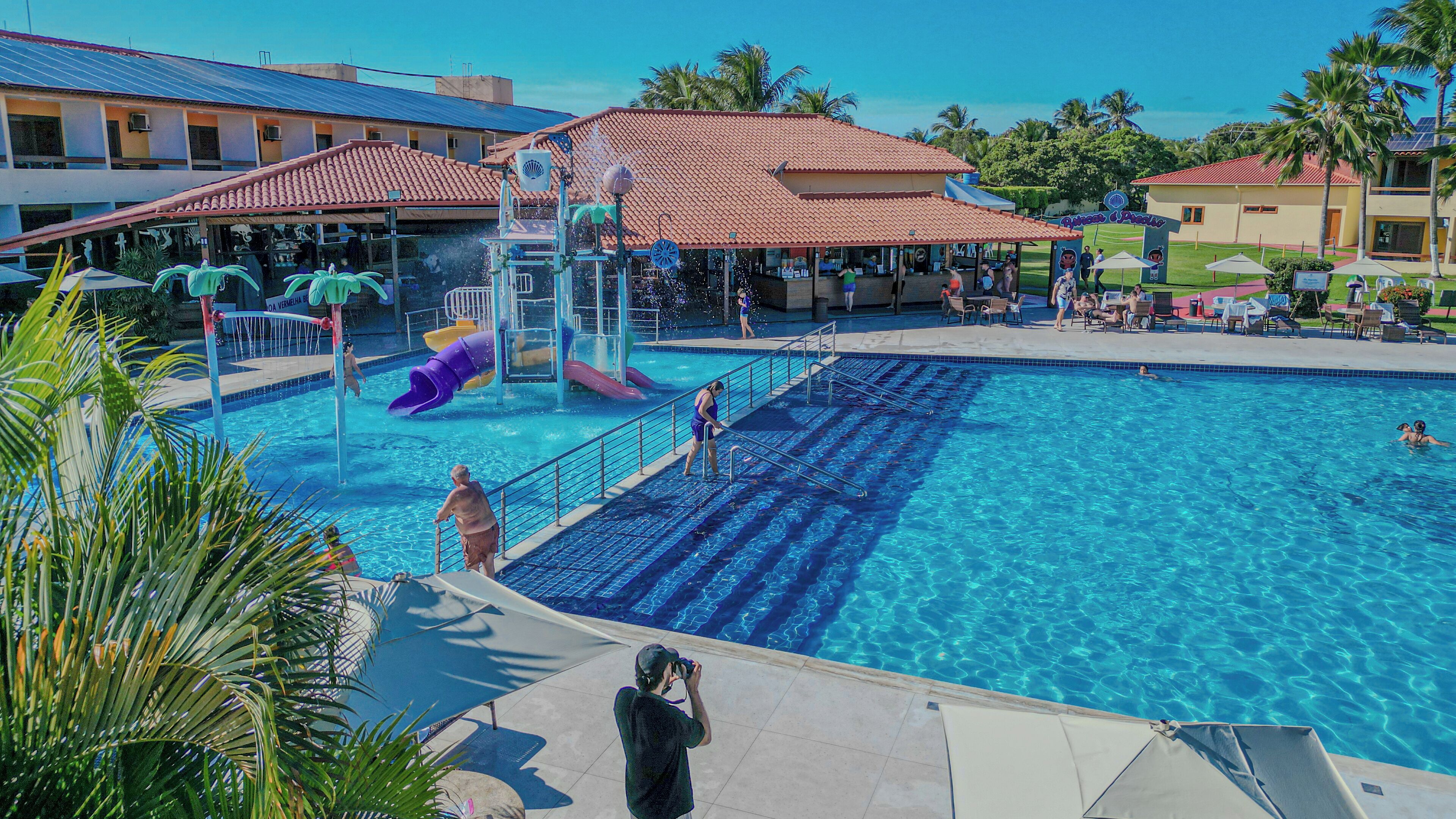 A swimming pool with a water slide, lounge chairs, and a covered area with a red roof.