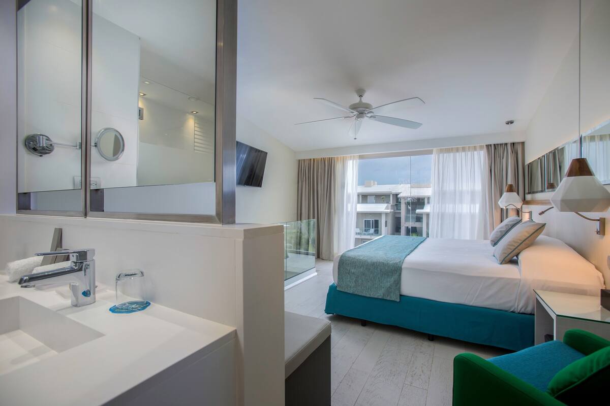 Ein Hotelzimmer mit einem großen Bett, einer separaten Sitzecke, einem Badezimmer mit Spiegel und Waschbecken sowie Blick auf die Stadt.