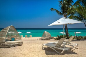 A beach with white lounge chairs, a white umbrella, and a wicker cabana. - Catalonia Royal La Romana - All Inclusive - Adults Only (San Rafael del Yuma)