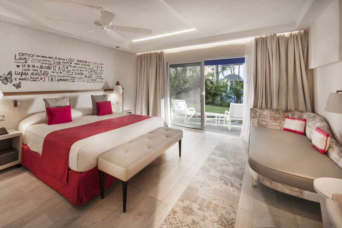 Ein modernes Hotelzimmer mit einem großen Bett, einer Bank, einem Sofa und einem Balkon mit Gartenmöbeln.