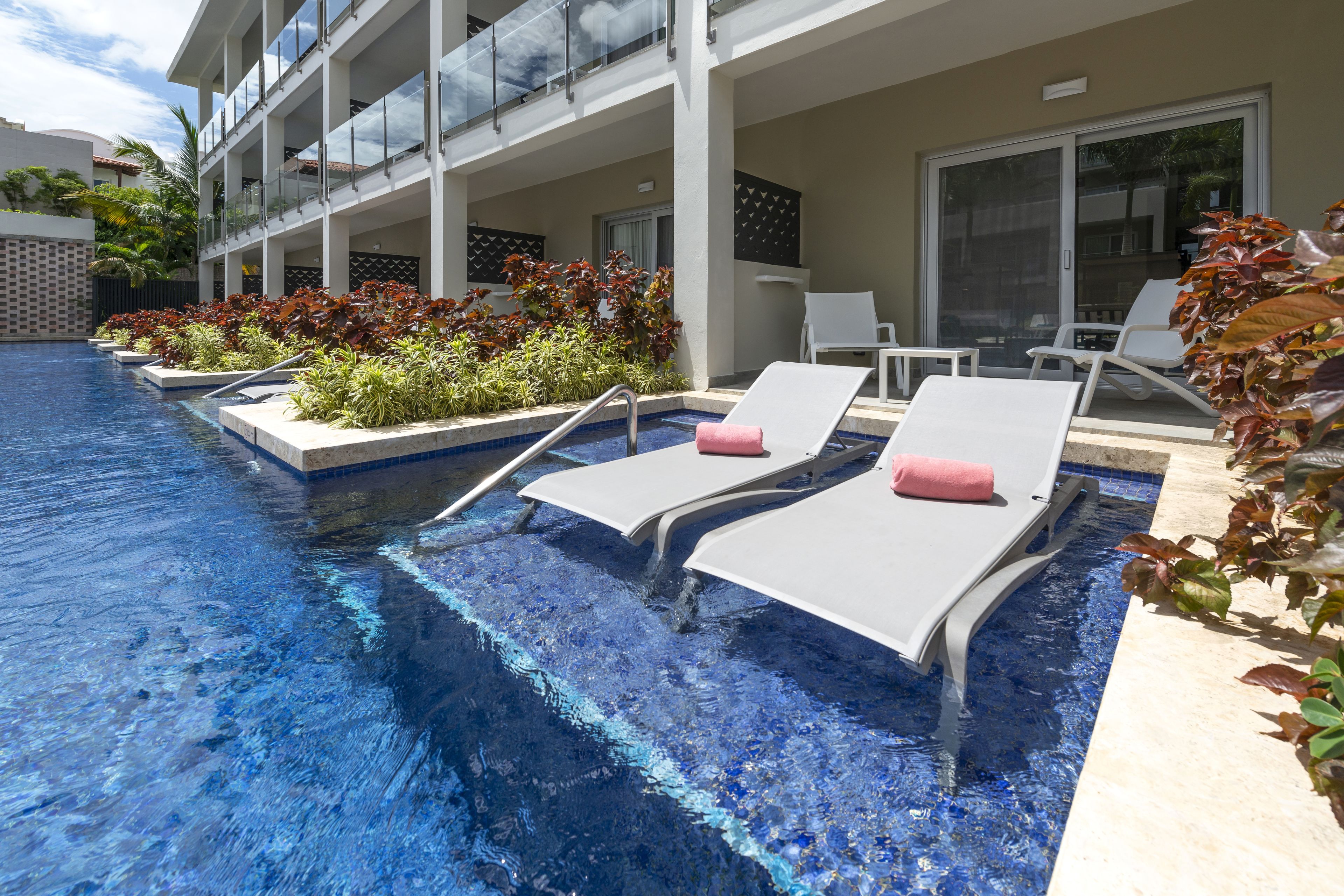 Un espace piscine avec des chaises longues, une balustrade en verre et un bâtiment à la façade recouverte de carreaux.