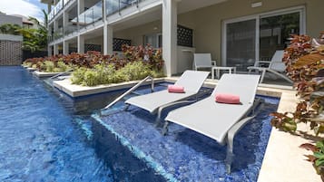 Un espace piscine avec des chaises longues, une balustrade en verre et un bâtiment à la façade recouverte de carreaux.