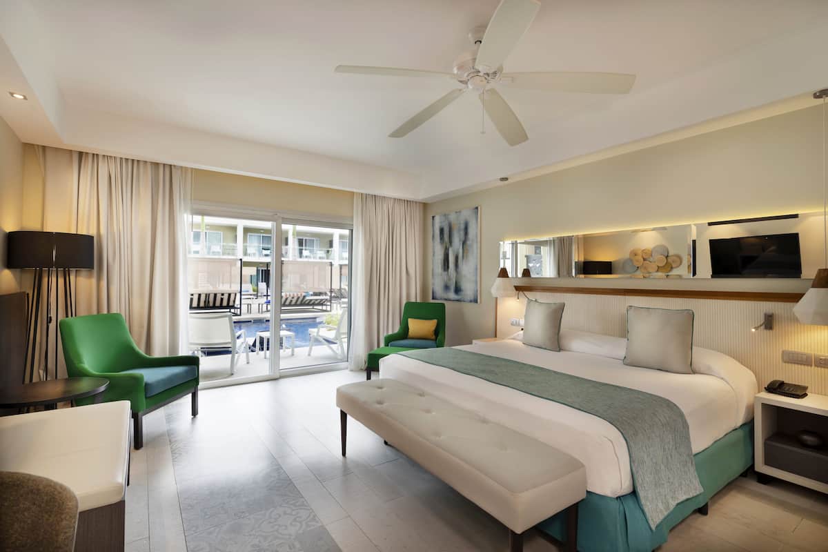 Ein modernes Hotelzimmer mit einem großen Bett, einem Deckenventilator, einem Fernseher und einem Balkon mit Sitzgelegenheit.