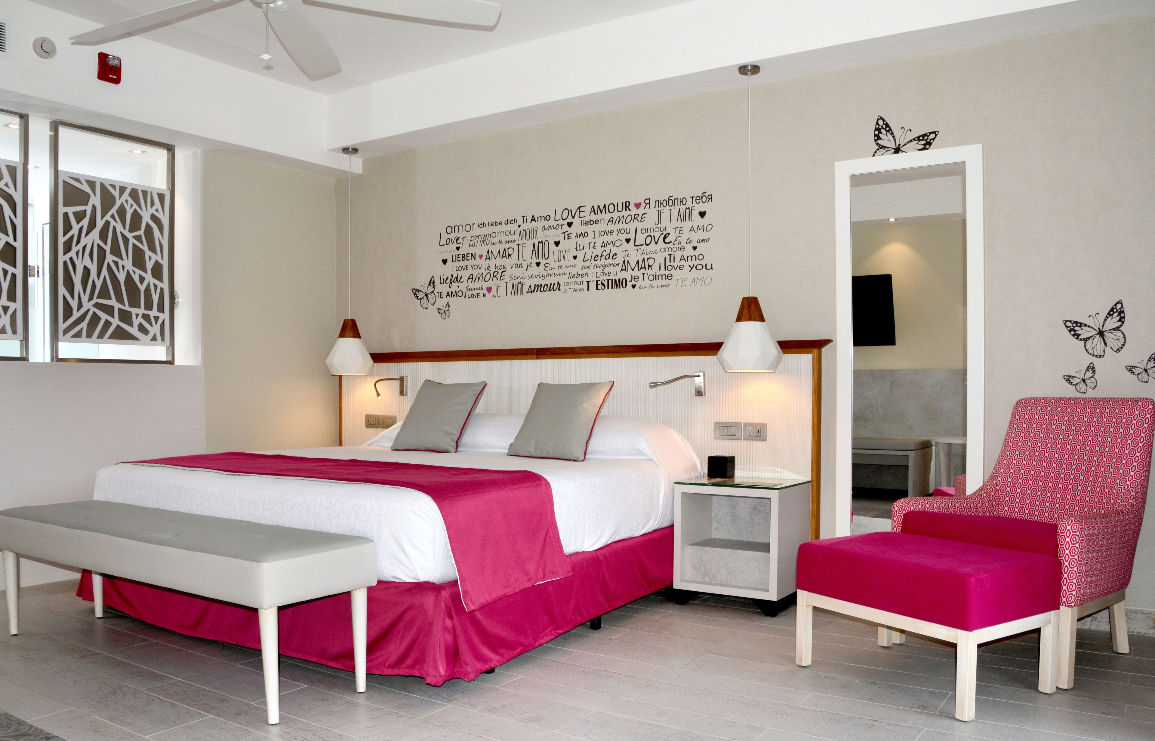 A modern hotel room with a large bed, bedside tables, a bench, a red armchair, and a wall with a butterfly decal.