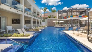 Una piscina con sillas de descanso y una zona de bar, rodeada de edificios de varios pisos con balcones.