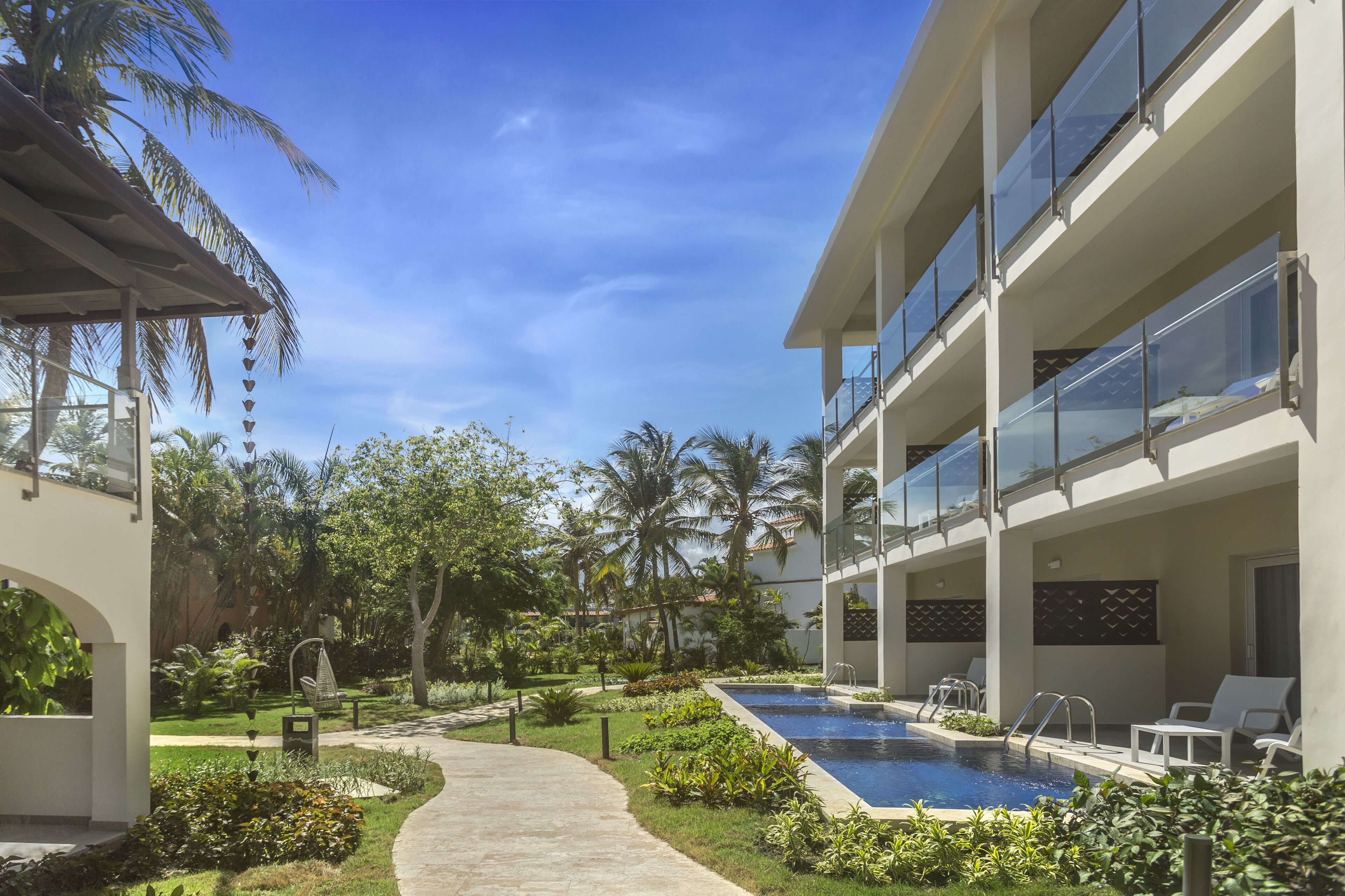 Un hotel moderno con piscina, abundante vegetación y cielo azul despejado.