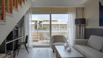 A modern living room with a sofa, a coffee table, and a TV. There is a balcony with a view of buildings.