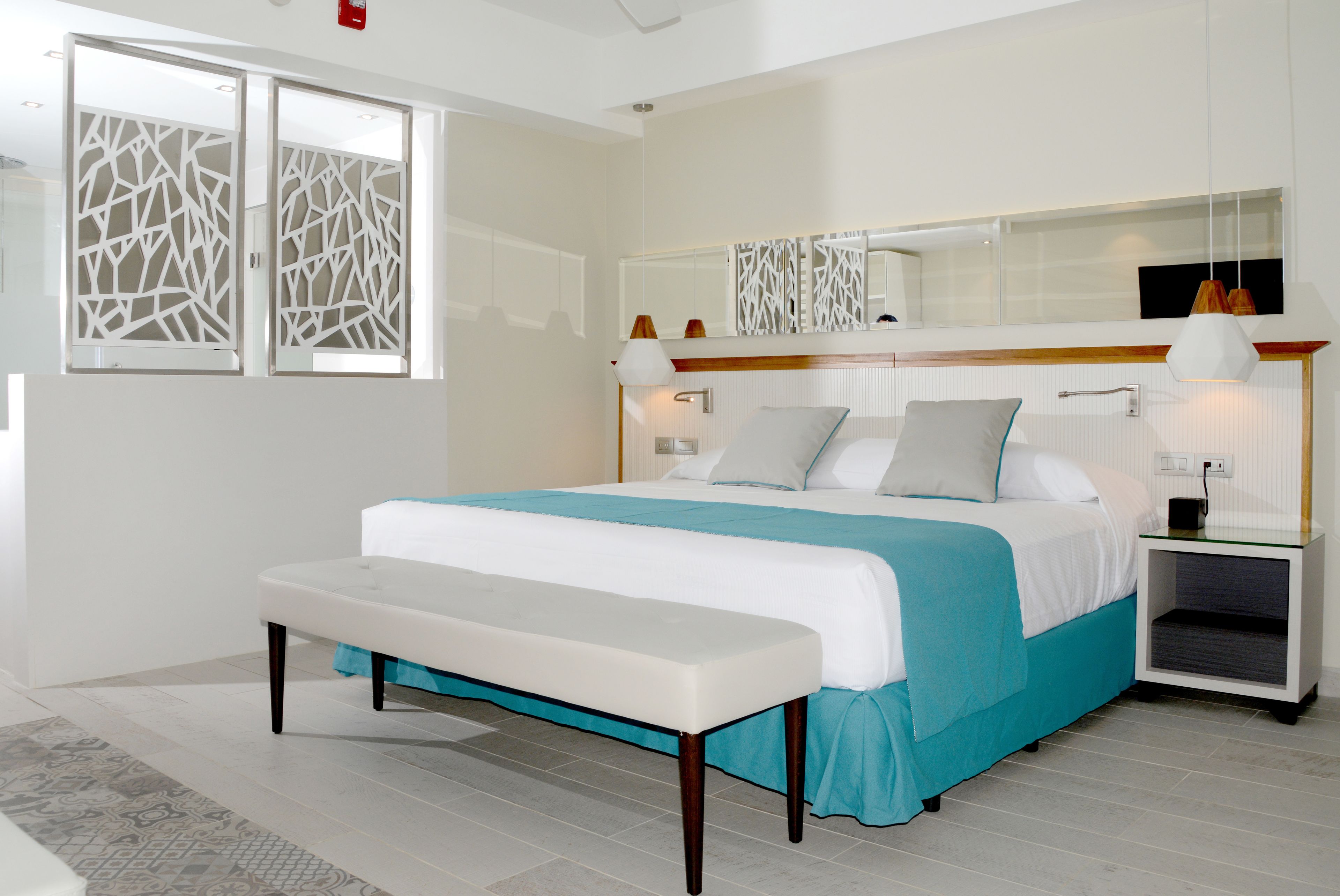 Quarto moderno com uma cama grande, um banco, uma mesinha de cabeceira e um espelho sobre a cama.