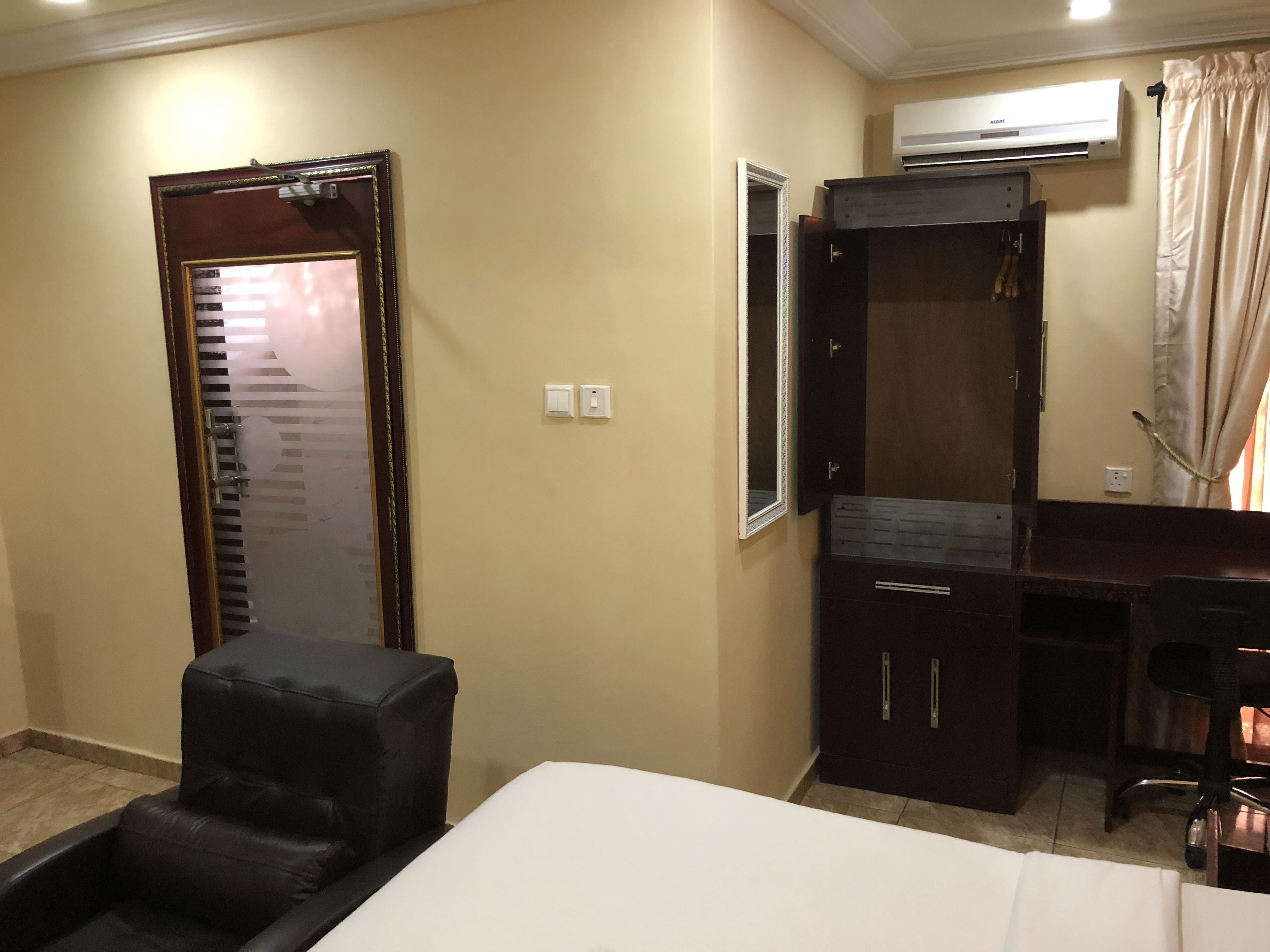 Habitación de hotel con cama, escritorio, silla, armario y unidad de aire acondicionado.