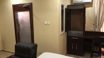 Habitación de hotel con cama, escritorio, silla, armario y unidad de aire acondicionado.