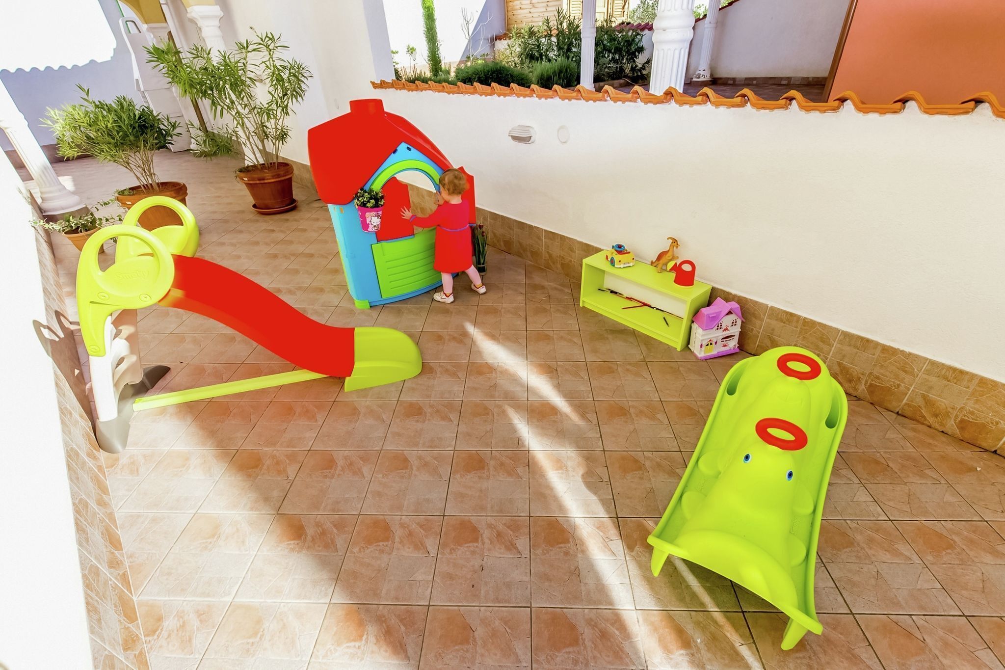 Ein Kinderspielbereich mit Rutsche, einem kleinen Haus und einem grünen Spielzeugauto.