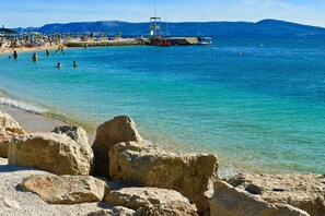 A beach with clear turquoise water, rocky foreground, and a pier with people and boats. - Villa in Croatia with Pool near Beach (Dramalj)
