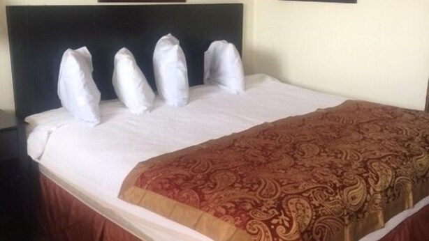 A hotel room with a large bed, a dark headboard, a red and gold patterned bedspread, and two framed pictures on the wall. - Park Motel (North Platte)